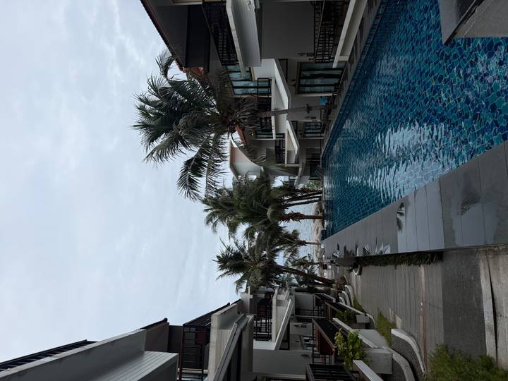 Serene resort pool lined with palm trees and modern villas with a glimpse of the sea beyond.