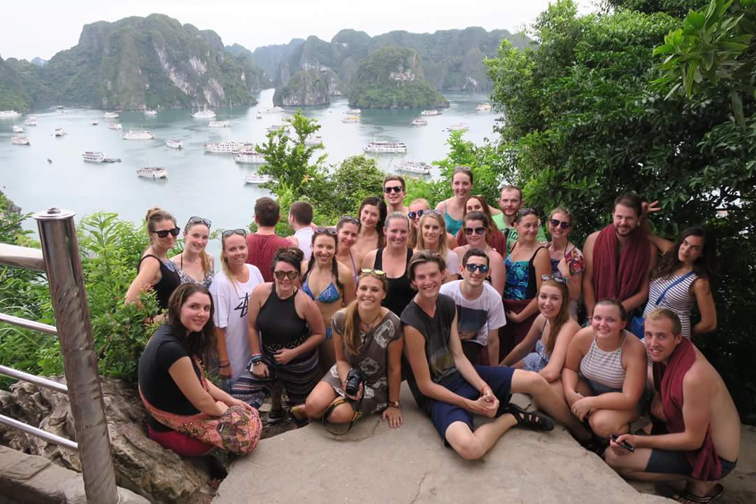 Grand groupe posant devant une vue panoramique de la baie avec des bateaux.