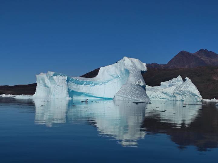 Massive blue-white iceberg floats serenely against rugged mountain backdrop.