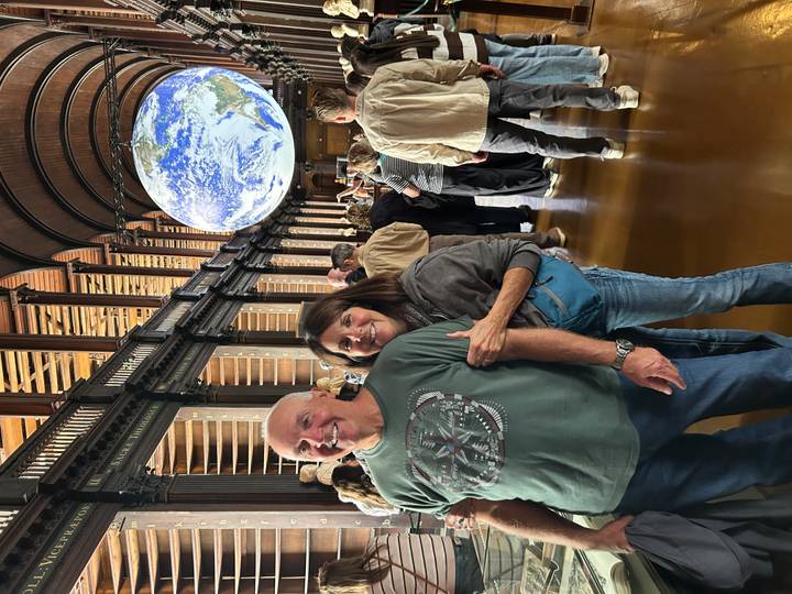 Visitors inside grand vaulted hall with giant suspended globe installation at Trinity College.