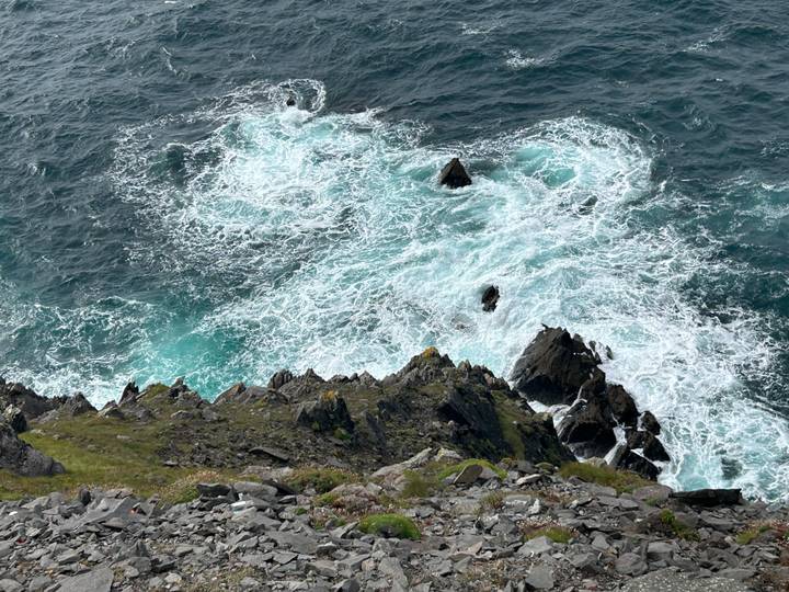 Top view of turquoise surf churning against jagged coastal rocks.