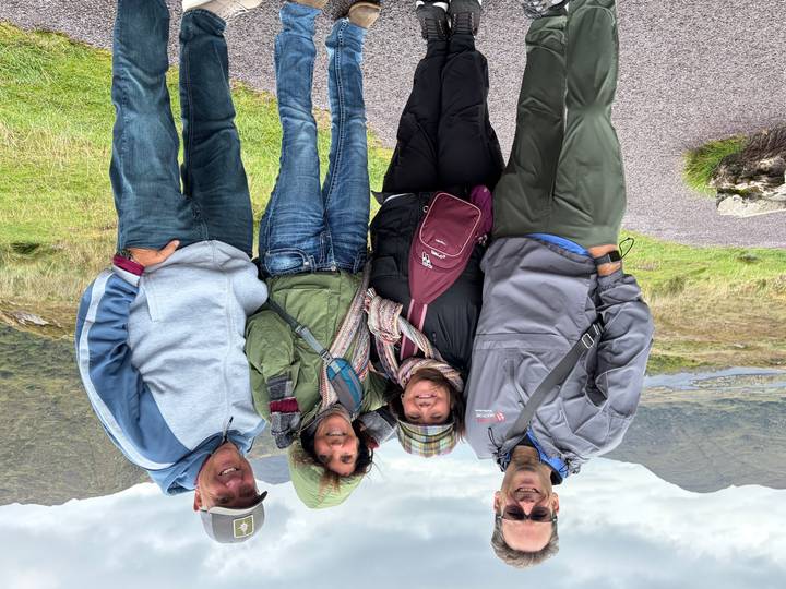 Four friends bundled in jackets posing in a windy highland landscape.