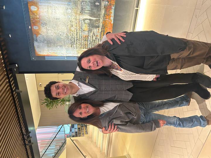 Two female travelers smiling beside a hotel staff member in modern lobby.