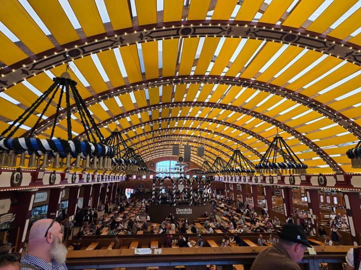 Wide view of a beer hall interior with striking yellow striped ceiling and hanging wreaths.