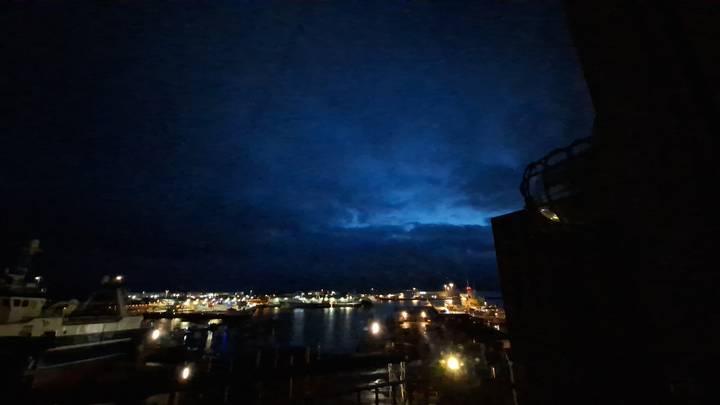 Nighttime harbour with distant city lights under a moody blue sky.