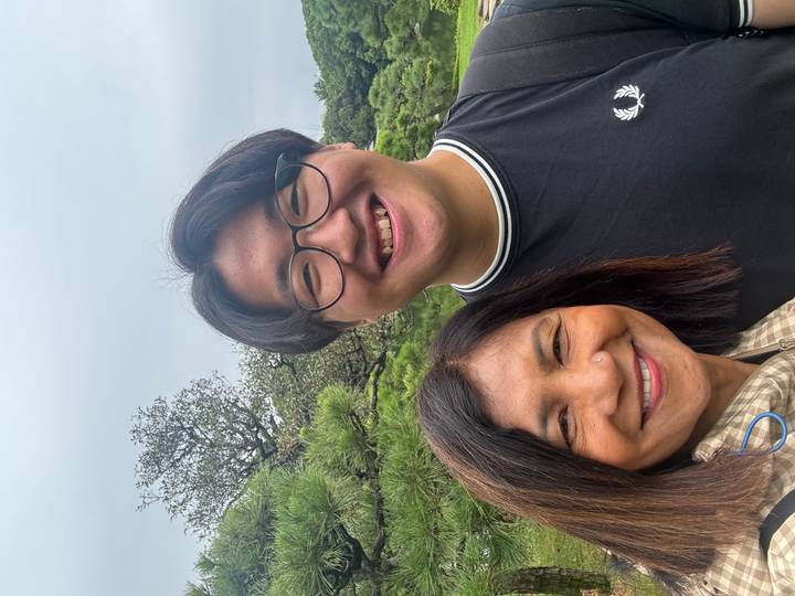 Close selfie of two travellers smiling in a Japanese garden with pine trees.