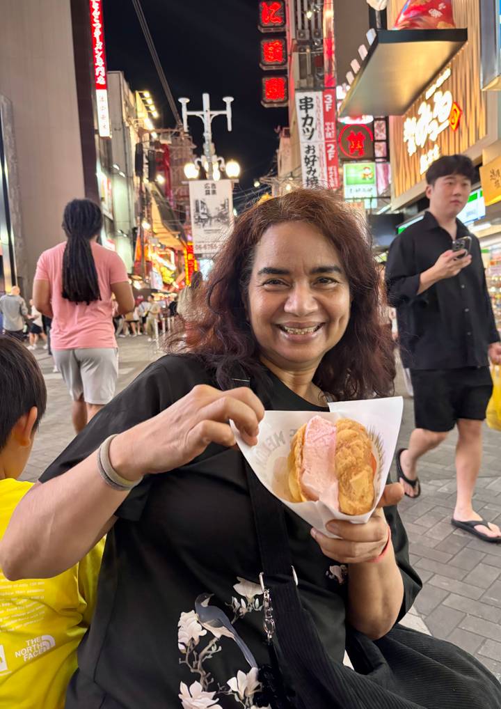 Woman enjoys a Japanese ice-cream sandwich on a busy neon-lit street.