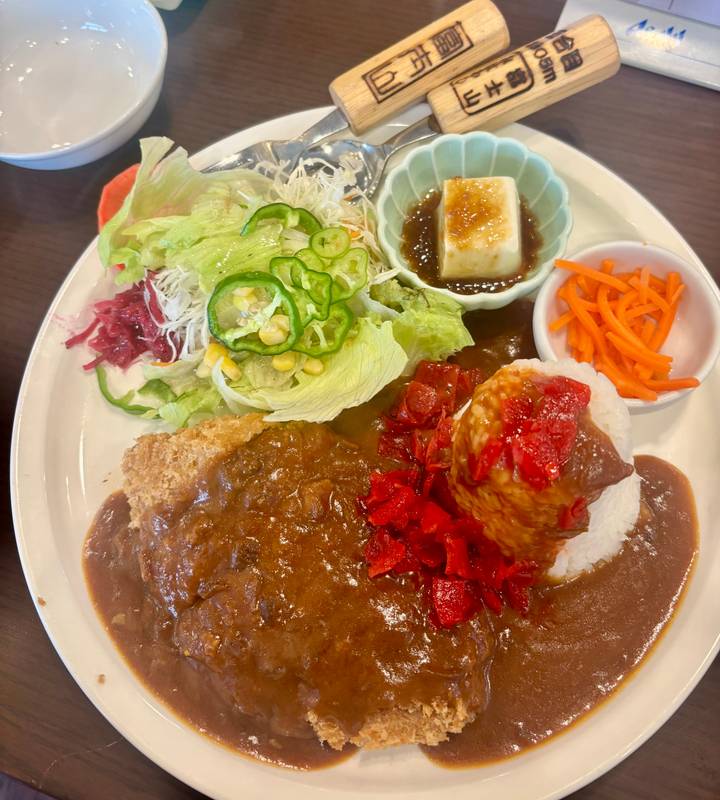 Colourful plate of Japanese curry rice with salad, pickles, tofu, and cutlet.