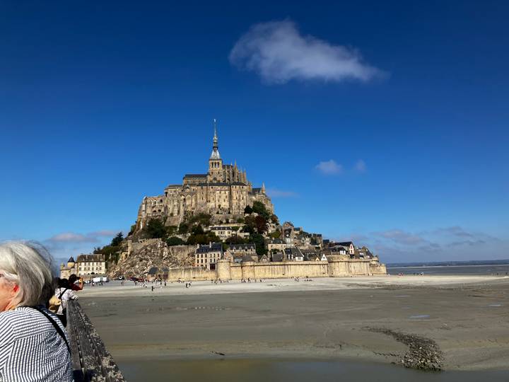 Iconic Mont Saint-Michel rising above vast tidal flats beneath a clear blue sky.
