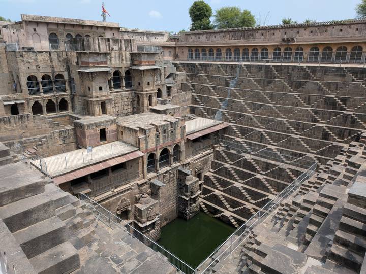 Intricate geometric steps of Chand Baori stepwell descending to green water.