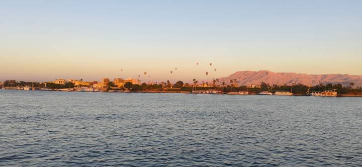 Early morning light bathes the Nile with distant balloons over a riverside town and desert mountains.