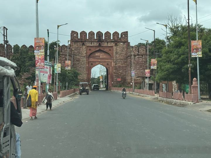 Stone city gate with vehicles and pedestrians on a cloudy day.