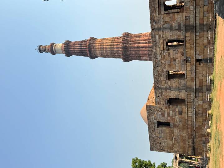 Qutub Minar rising beside ancient stone ruins under clear blue sky.