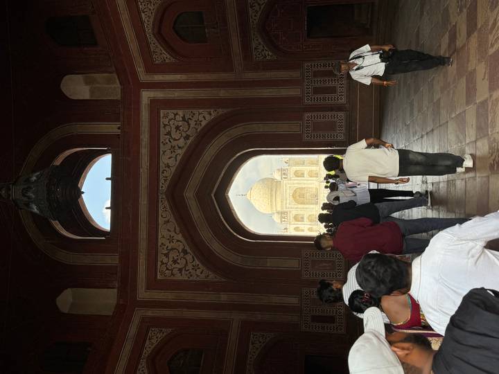 View of the Taj Mahal framed by a Mughal gateway crowded with visitors.