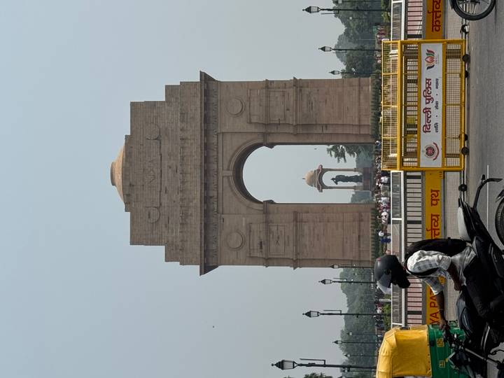 India Gate monument on hazy day with motorbike and barricades in foreground.