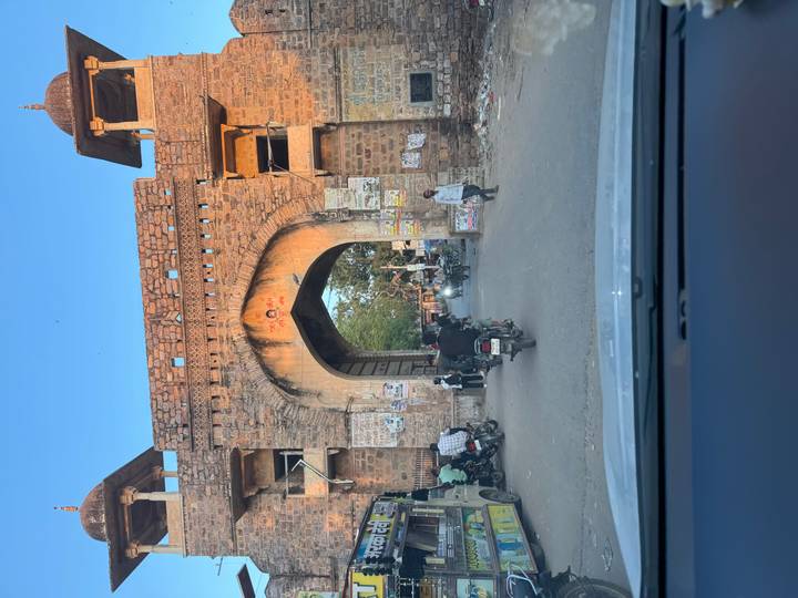 Vehicles and pedestrians passing through a rustic stone gate at dusk.