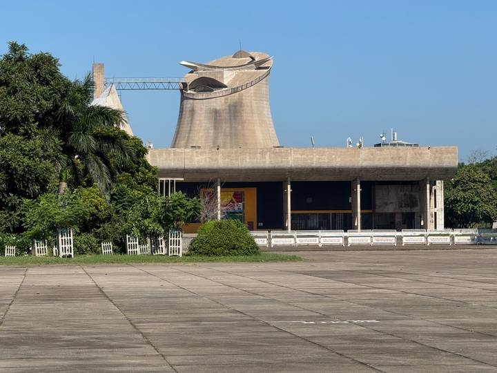 Distinctive concrete tower and assembly building of Chandigarh framed by lush greenery on a sunny day.