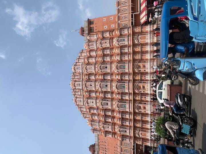 Street-level view of Jaipur’s Hawa Mahal with busy traffic of tuk-tuks and motorbikes in foreground.