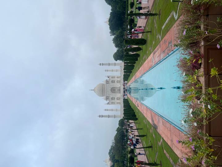 Classic symmetrical view of the Taj Mahal with reflecting pool and trimmed gardens under hazy sky.