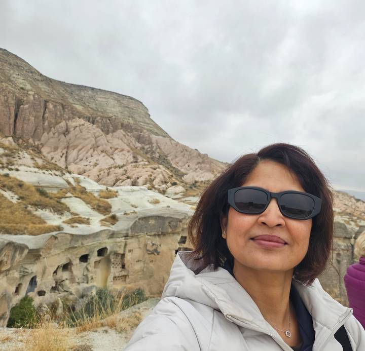 Selfie of traveller wearing sunglasses with Cappadocia’s pink rock formations and cave dwellings behind.