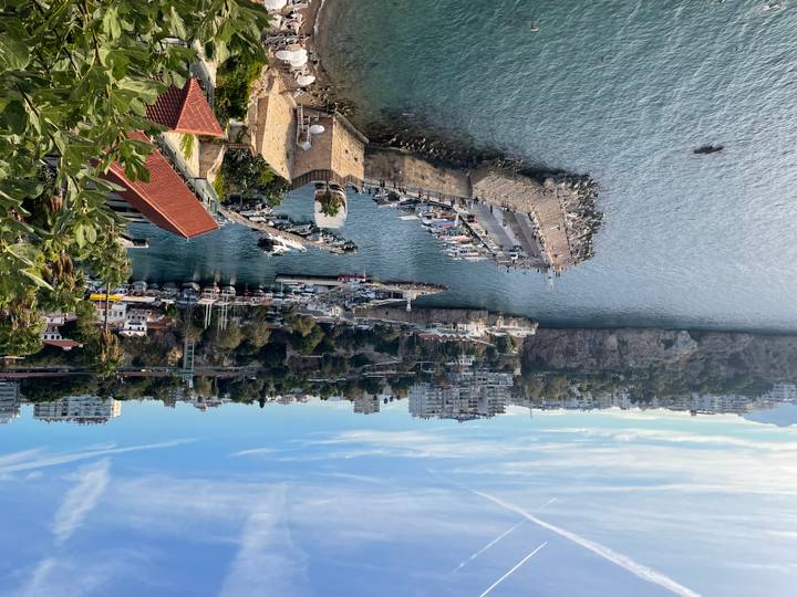 Scenic view over Antalya’s old harbor with stone walls, docked boats and coastal cliffs under a clear blue sky.