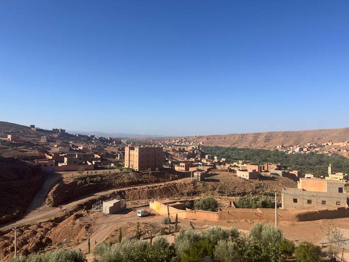 Terracotta-coloured village houses scatter across a dry hillside overlooking a narrow green valley.