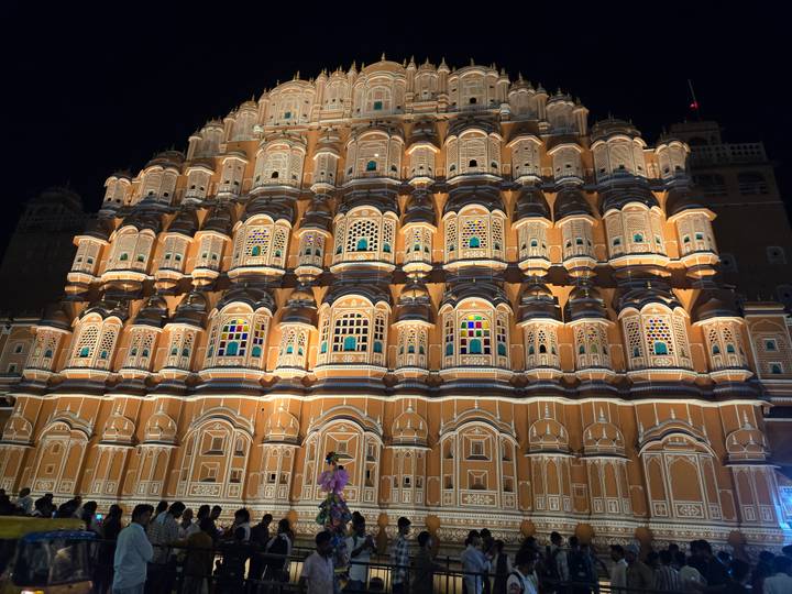 Hawa Mahal palace illuminated beautifully at night with a single visitor in front.