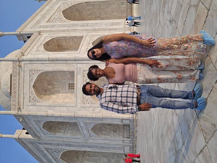 Guide and two travelers pose in front of the Taj Mahal wearing protective shoe covers.