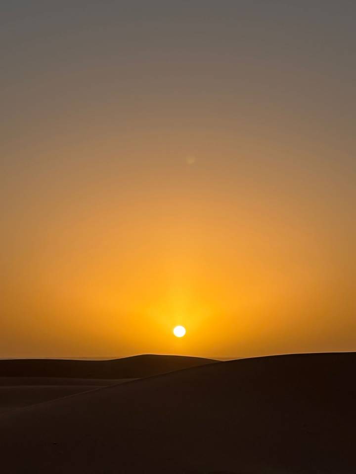 Minimalist image of a glowing orange sun just above the horizon in a clear sky.