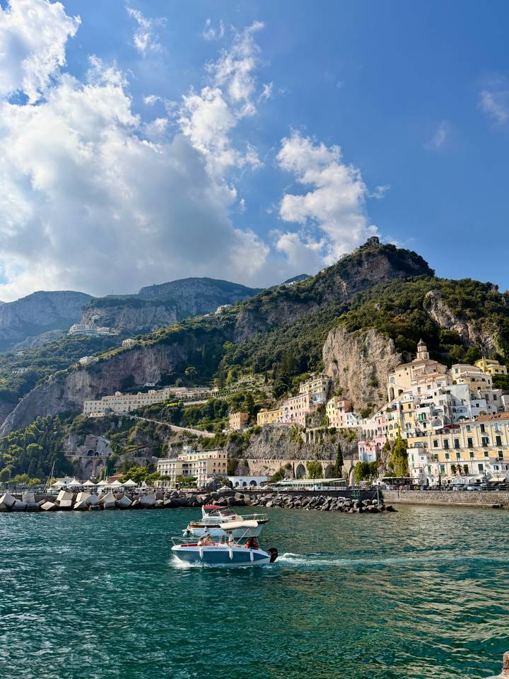 Colorful Amalfi Coast village clings to steep cliffs beneath towering mountains.