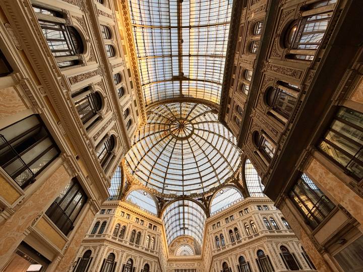 Grand glass-domed arcade ceiling of a 19th-century shopping gallery lit by warm light.
