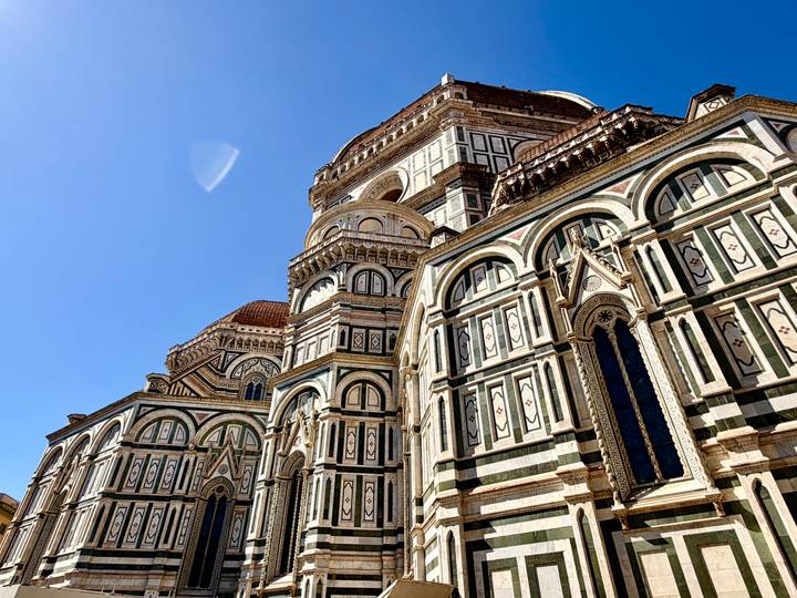Ornate marble façade and dome of Florence’s Duomo under a deep blue sky