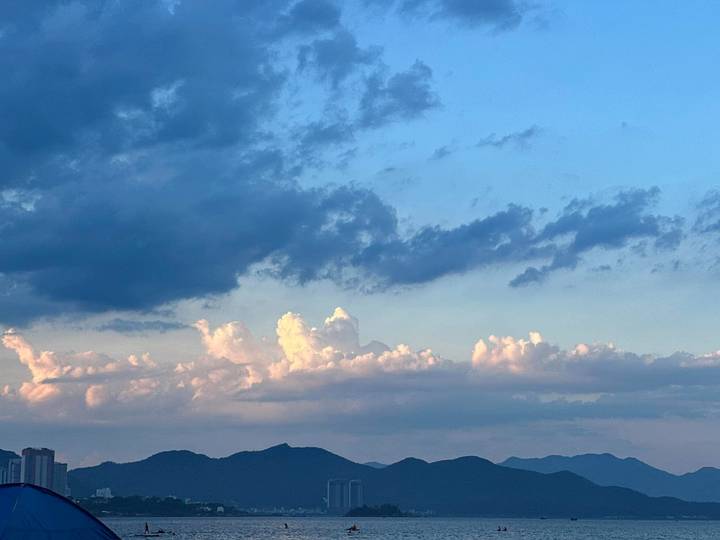 Evening sky with dramatic clouds over distant mountains and a sliver of city skyline.