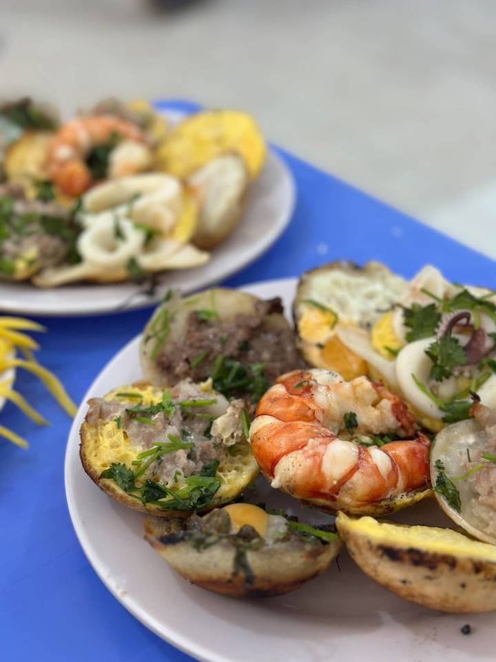 Close view of Vietnamese street-food plate with shrimp, squid, and savory pancakes garnished with herbs.