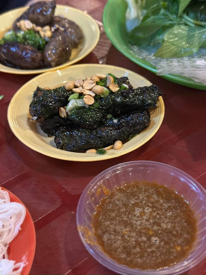 Vietnamese dish of grilled betel-leaf wrapped meat topped with peanuts on a small plate.