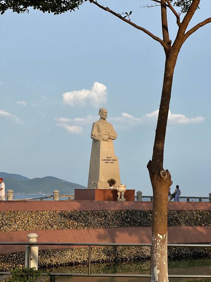 Statue of Alexandre Yersin stands by the seaside promenade under a sunny sky.