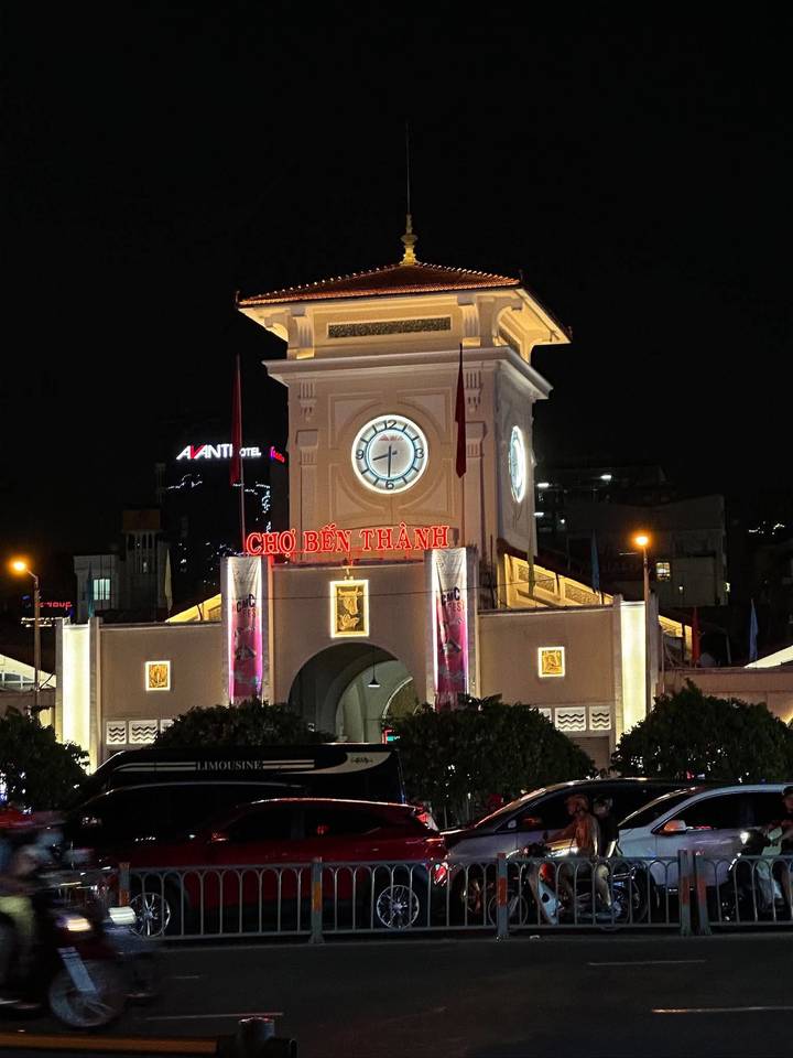 Night view of Bến Thành Market clock tower lit with neon signage in Ho Chi Minh City.