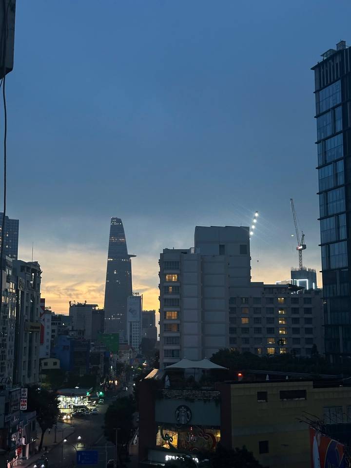 City skyline at dusk with the distinctive Bitexco Financial Tower and construction cranes silhouetted.