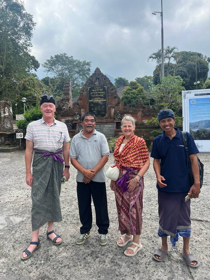 Four adults pose in front of a sign for Pura Luhur Batukaru with temple gate behind.