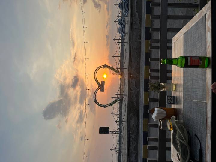 Romantic beachside table view of a heart-shaped frame catching the setting sun over the sea.