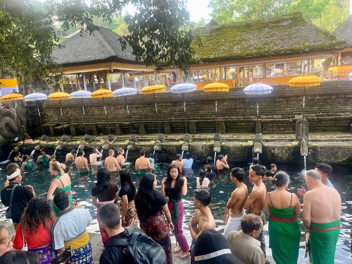 Crowd of worshippers bathe beneath holy spouts in a stone pool at a sacred temple.