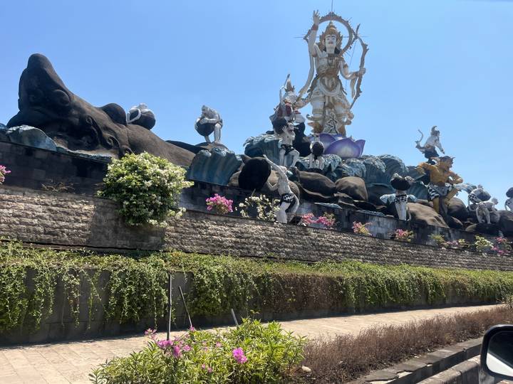 Massive mythological statue ensemble with flowers against a bright blue sky.