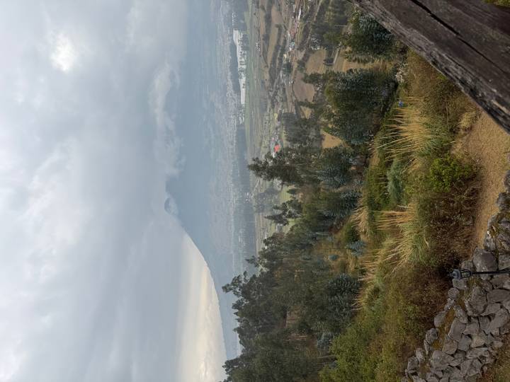 Misty valley view of a dormant volcano rising above patchwork farmland under gray skies.