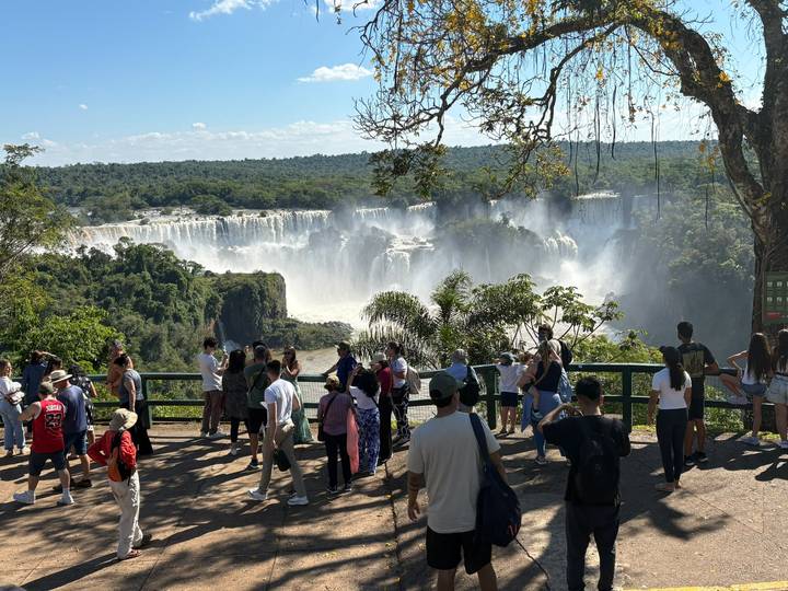 Crowds at a panoramic viewpoint admire the vast Iguazu Falls amid mist and rainforest.