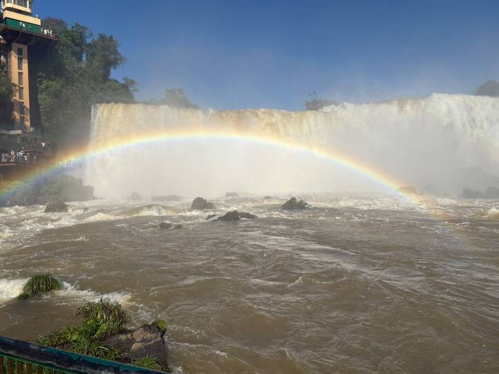Vibrant rainbow arches over the rushing brown waters at the base of Iguazu Falls.