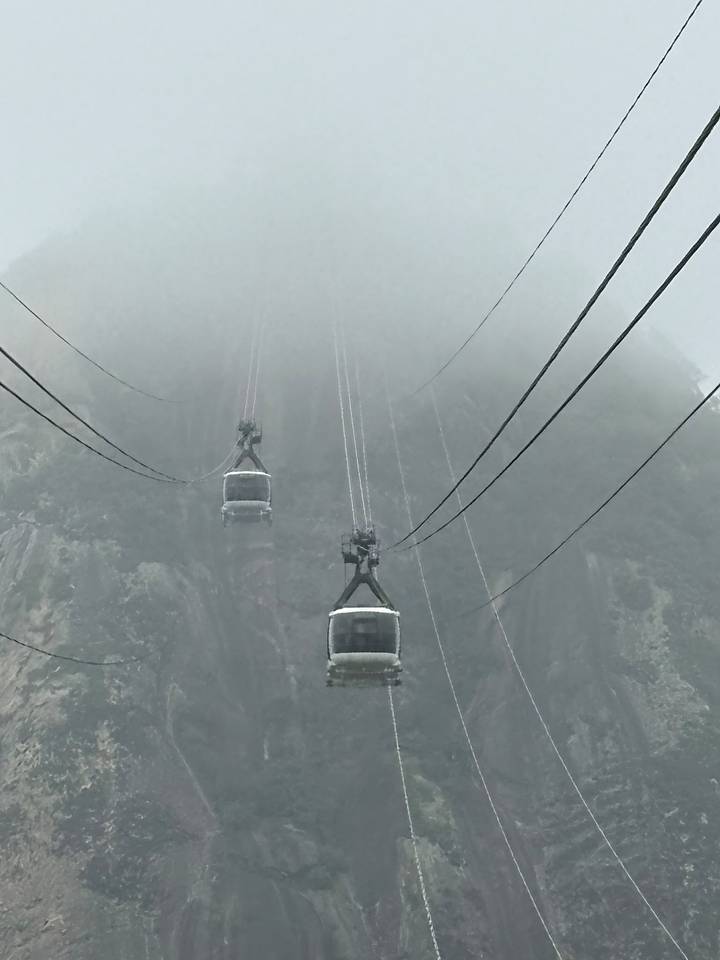 Cable cars disappear into thick fog on a steep granite mountain face.