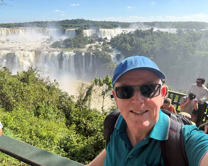 Selfie of a traveller in sunglasses overlooking Iguazu Falls from a forested viewpoint.