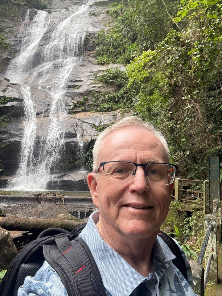 Selfie of traveller with a gentle jungle waterfall cascading behind him.