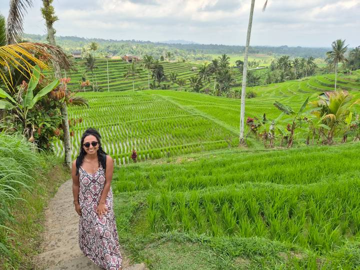 Woman smiles beside vivid green stepped rice terraces stretching across the valley landscape.