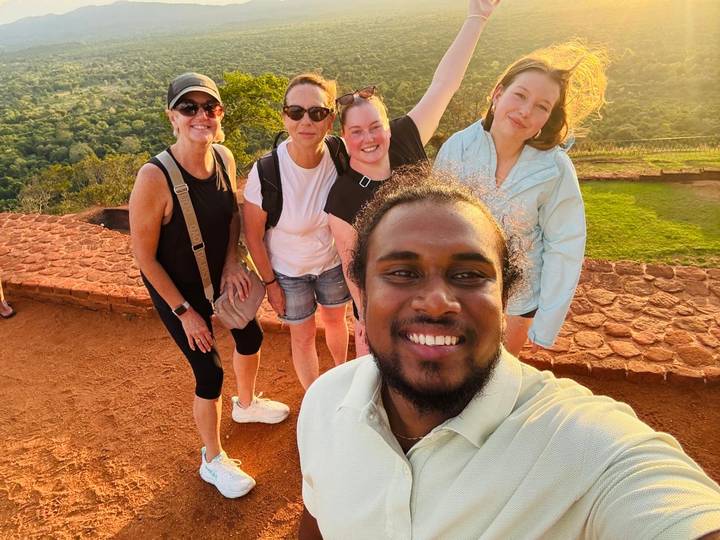 A smiling group selfie on a rocky viewpoint overlooking lush Sri Lankan countryside.